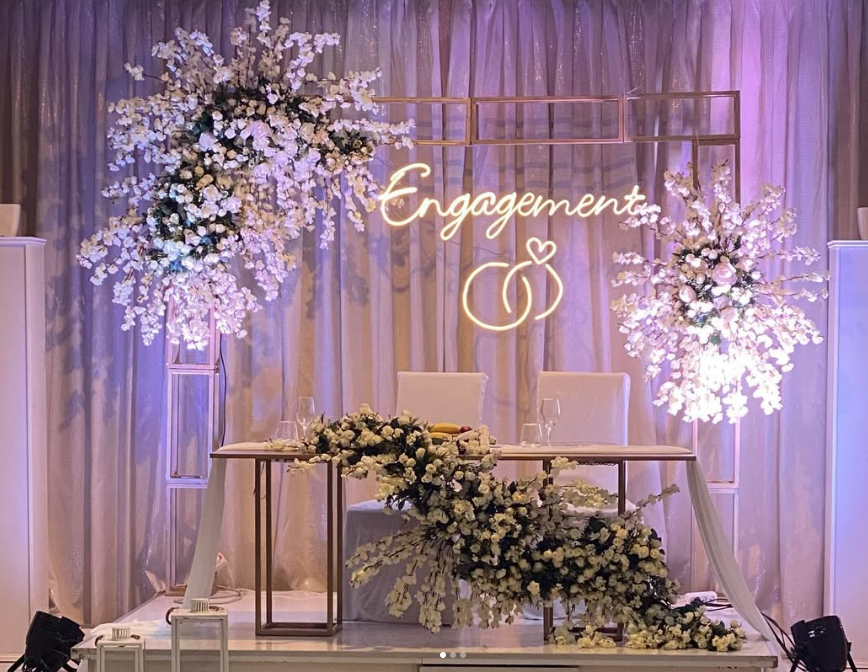Engagement stage with white flowers and illuminated ring sign.