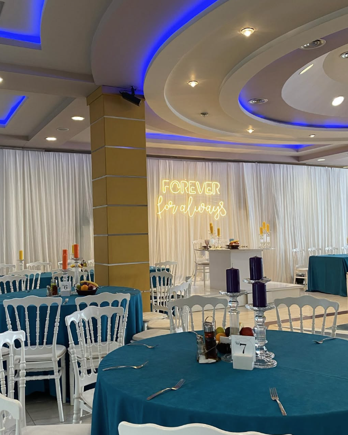 Wedding hall with blue tablecloths and a glowing forever sign.